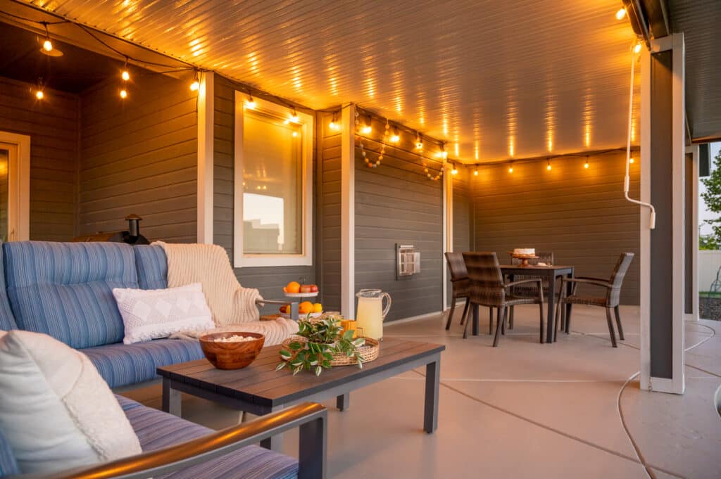 beautiful grey and white patio cover with blue patio furniture and string lights